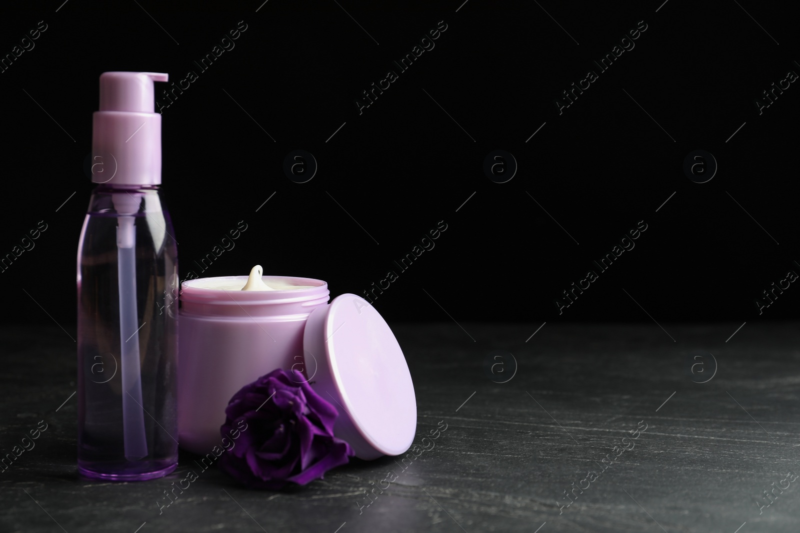 Photo of Hair cosmetic products and flower on black stone table. Space for text