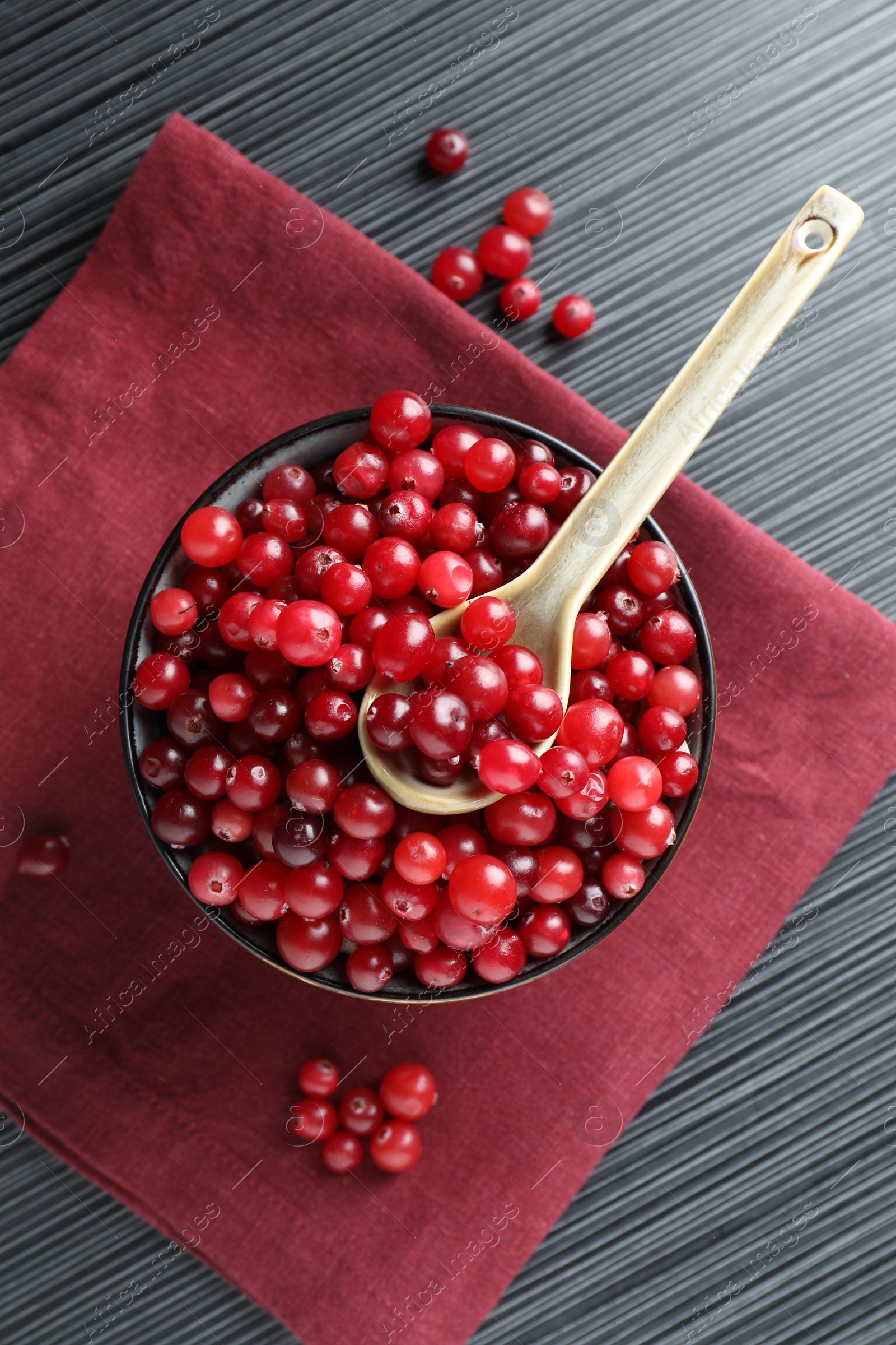 Photo of Cranberries in bowl and spoon on black wooden table, top view