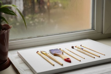 Photo of White canvas and different brushes on windowsill