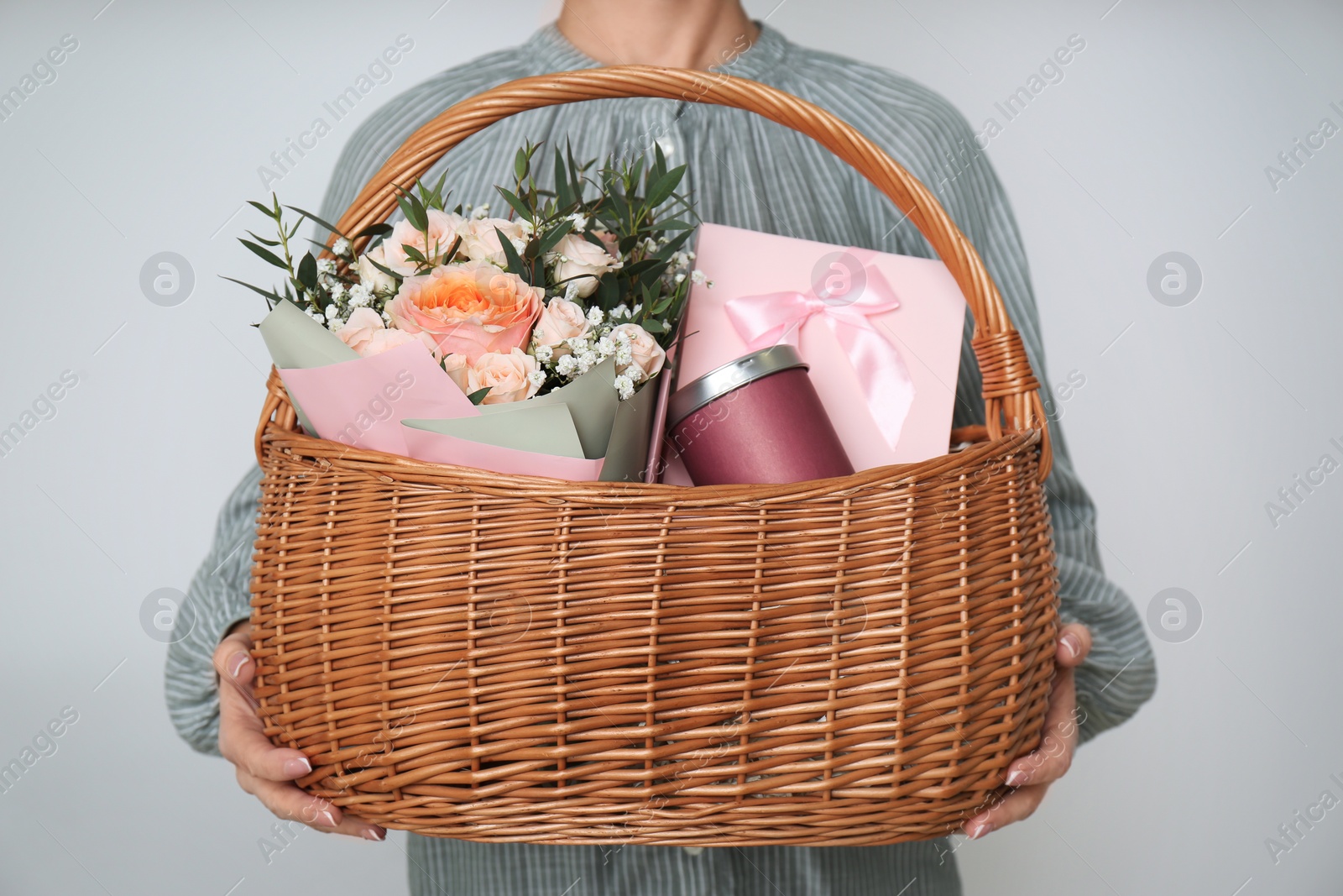 Photo of Woman holding wicker basket with different gifts on grey background, closeup