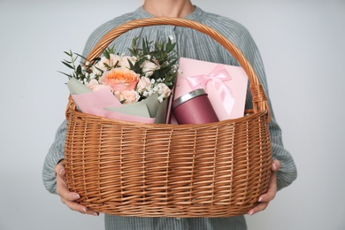 Photo of Woman holding wicker basket with different gifts on grey background, closeup