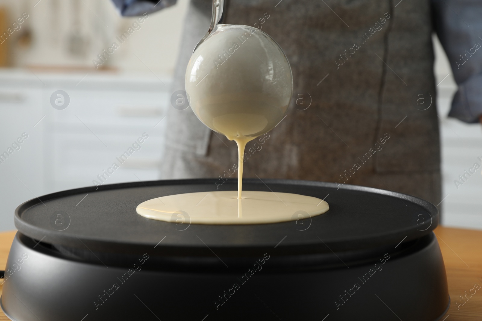 Photo of Woman cooking delicious crepe on electrical pancake maker in kitchen, closeup