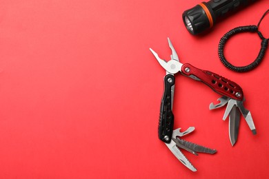 Photo of Compact portable multitool, bracelet and flashlight on red background, flat lay. Space for text