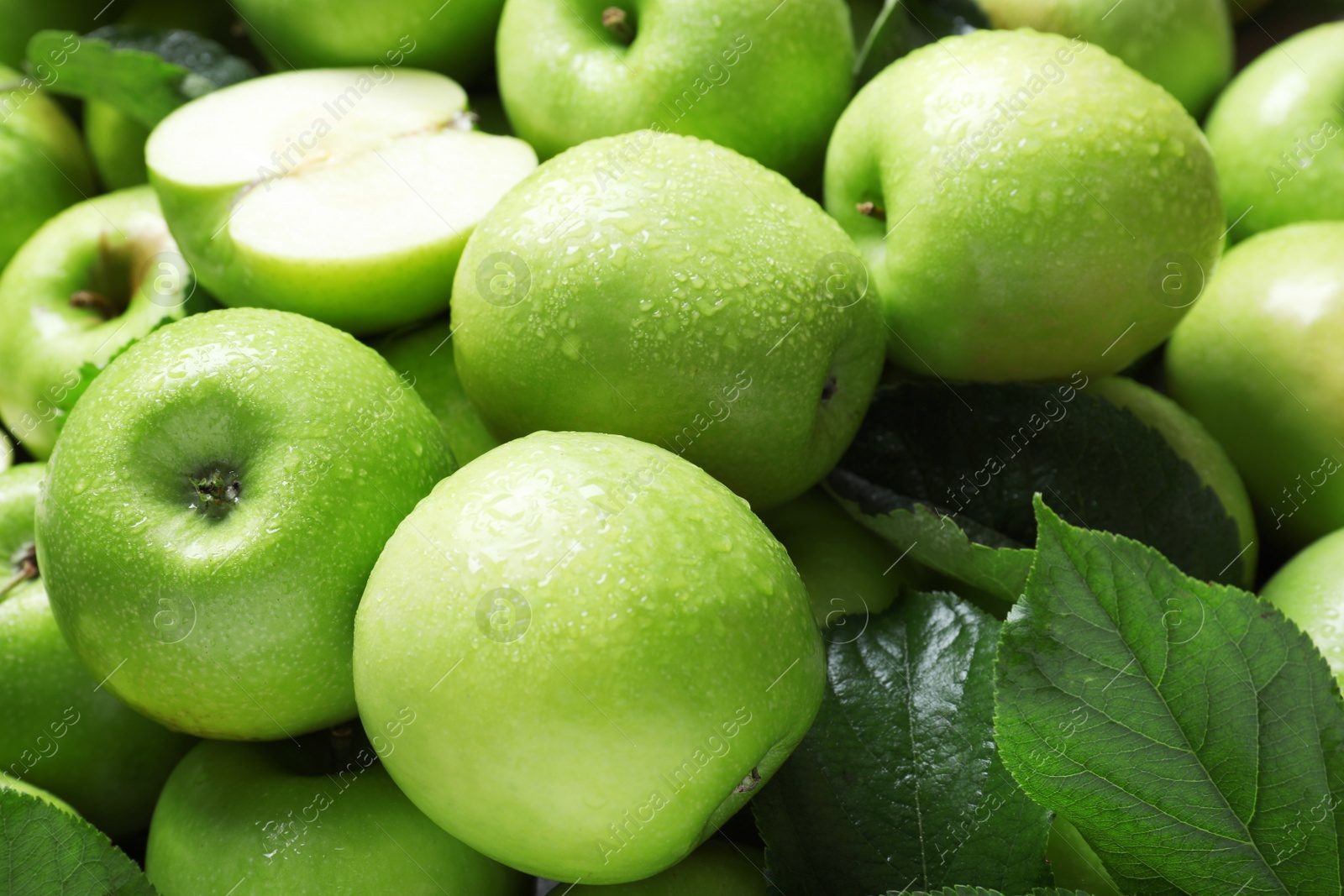 Photo of Pile of wet green apples with leaves as background, closeup