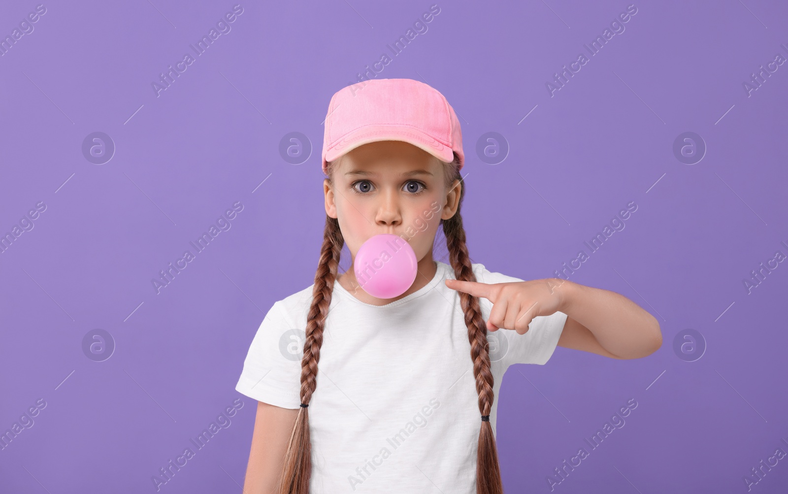 Photo of Surprised girl blowing bubble gum on purple background