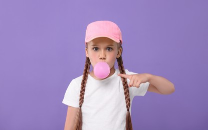 Surprised girl blowing bubble gum on purple background