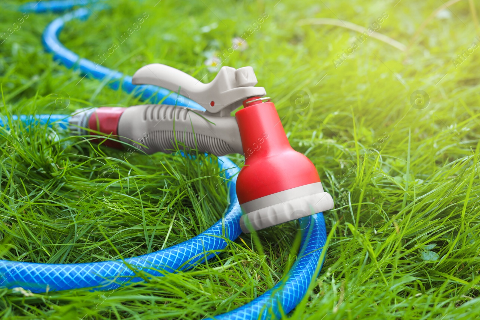 Photo of Watering hose with sprinkler on green grass outdoors, closeup