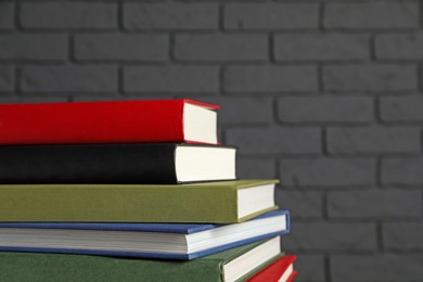 Photo of Stack of hardcover books near dark brick wall, closeup. Space for text