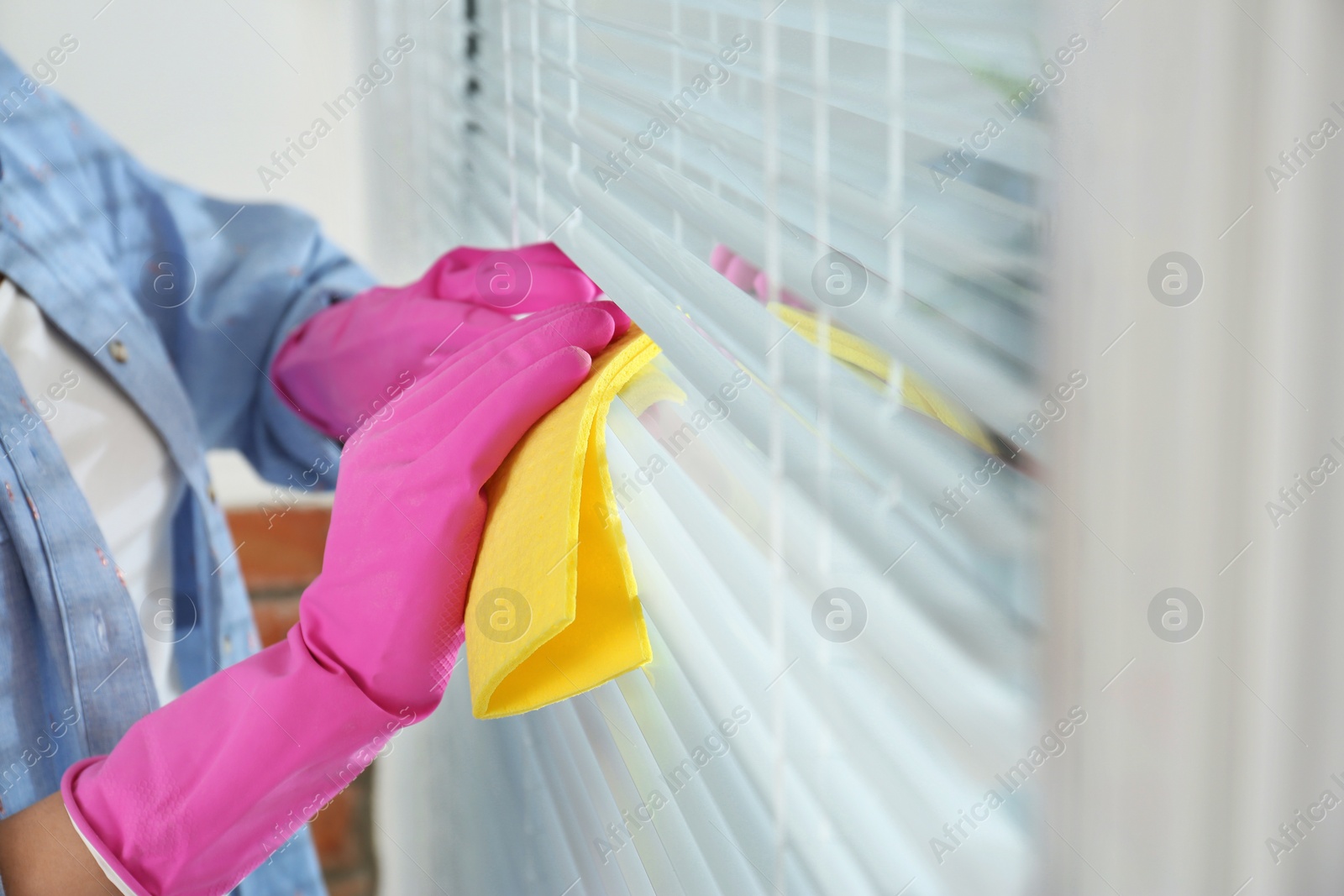 Image of Woman cleaning window blinds with rag indoors, closeup