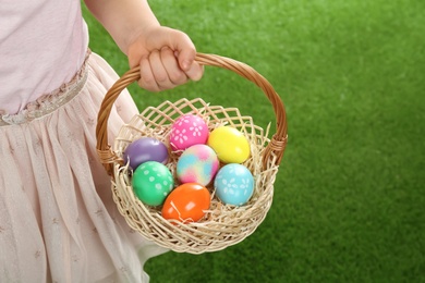 Photo of Little girl with basket full of Easter eggs on green grass, closeup. Space for text