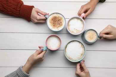 People holding different cups with aromatic hot coffee at white wooden table, top view