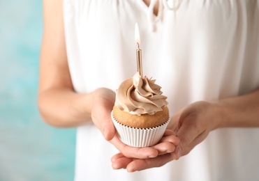 Woman holding delicious birthday cupcake with burning candle, closeup