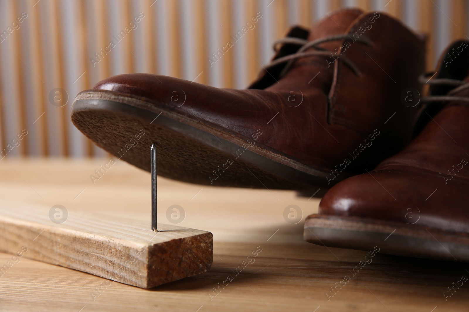 Photo of Metal nail in wooden plank and shoes on table, closeup