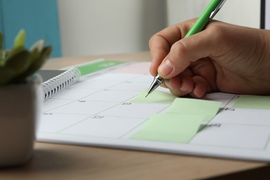 Photo of Timetable. Man making schedule using calendar and sticky note at table, closeup