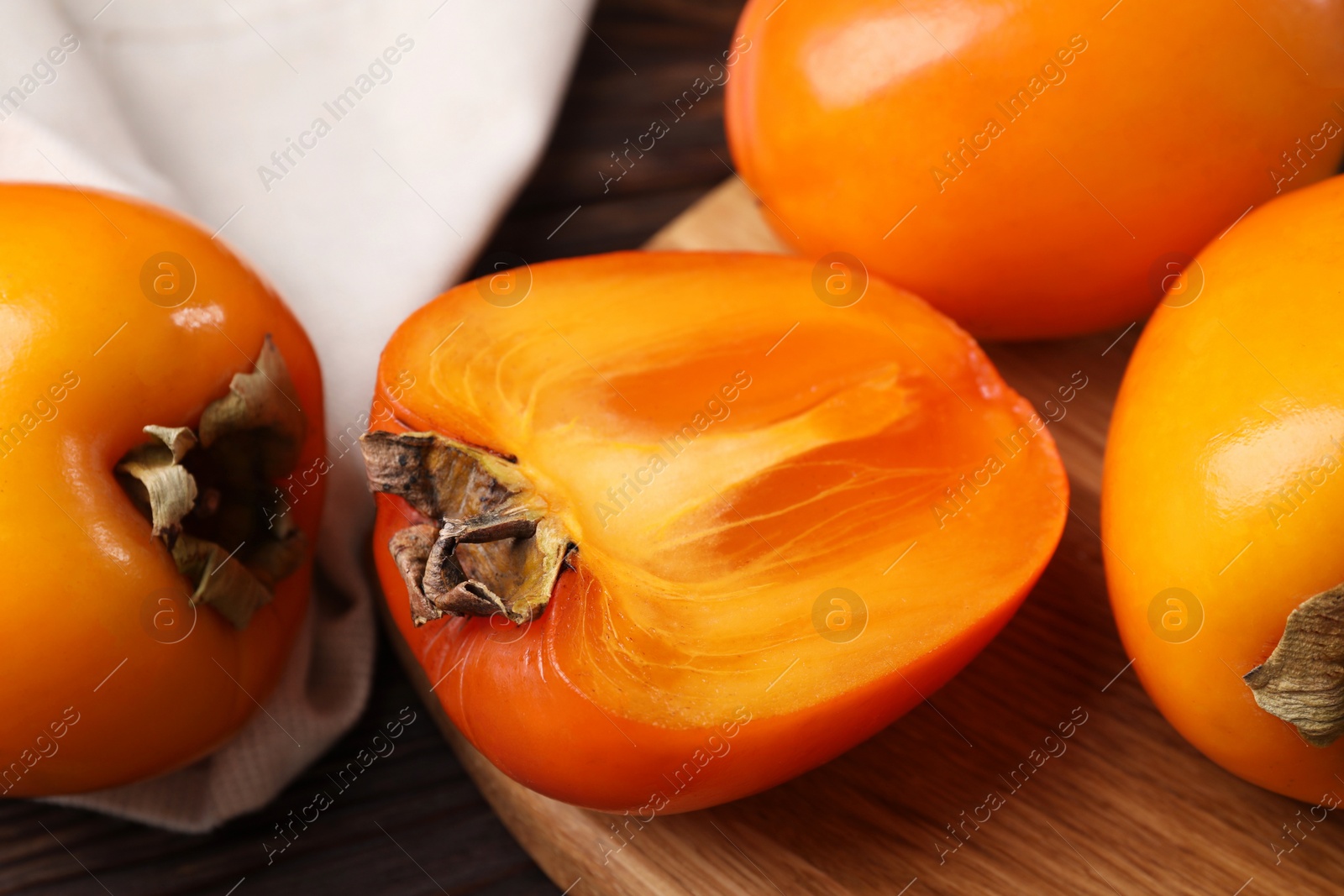 Photo of Whole and cut delicious ripe persimmons on wooden table, closeup