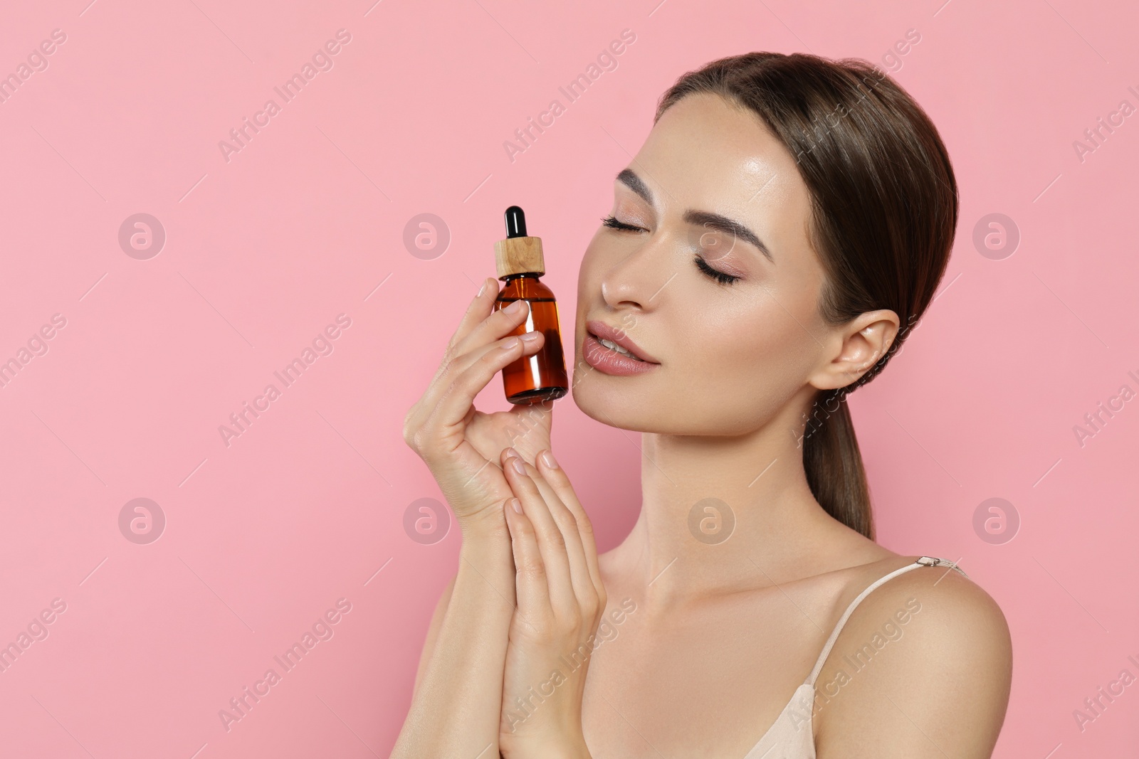 Photo of Young woman with bottle of essential oil on pink background, space for text