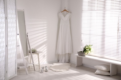 Photo of Beautiful wedding dress hanging on white wall in room
