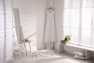 Beautiful wedding dress hanging on white wall in room