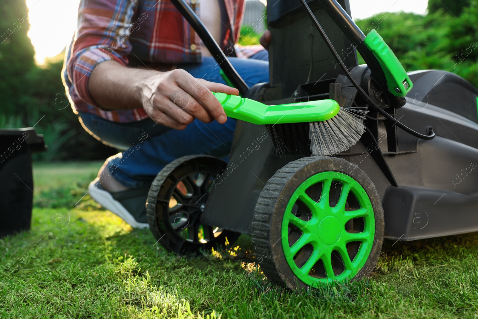 Photo of Man cleaning lawn mower with brush in garden, closeup