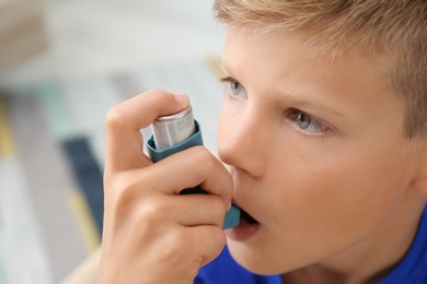 Little boy using asthma inhaler on blurred background