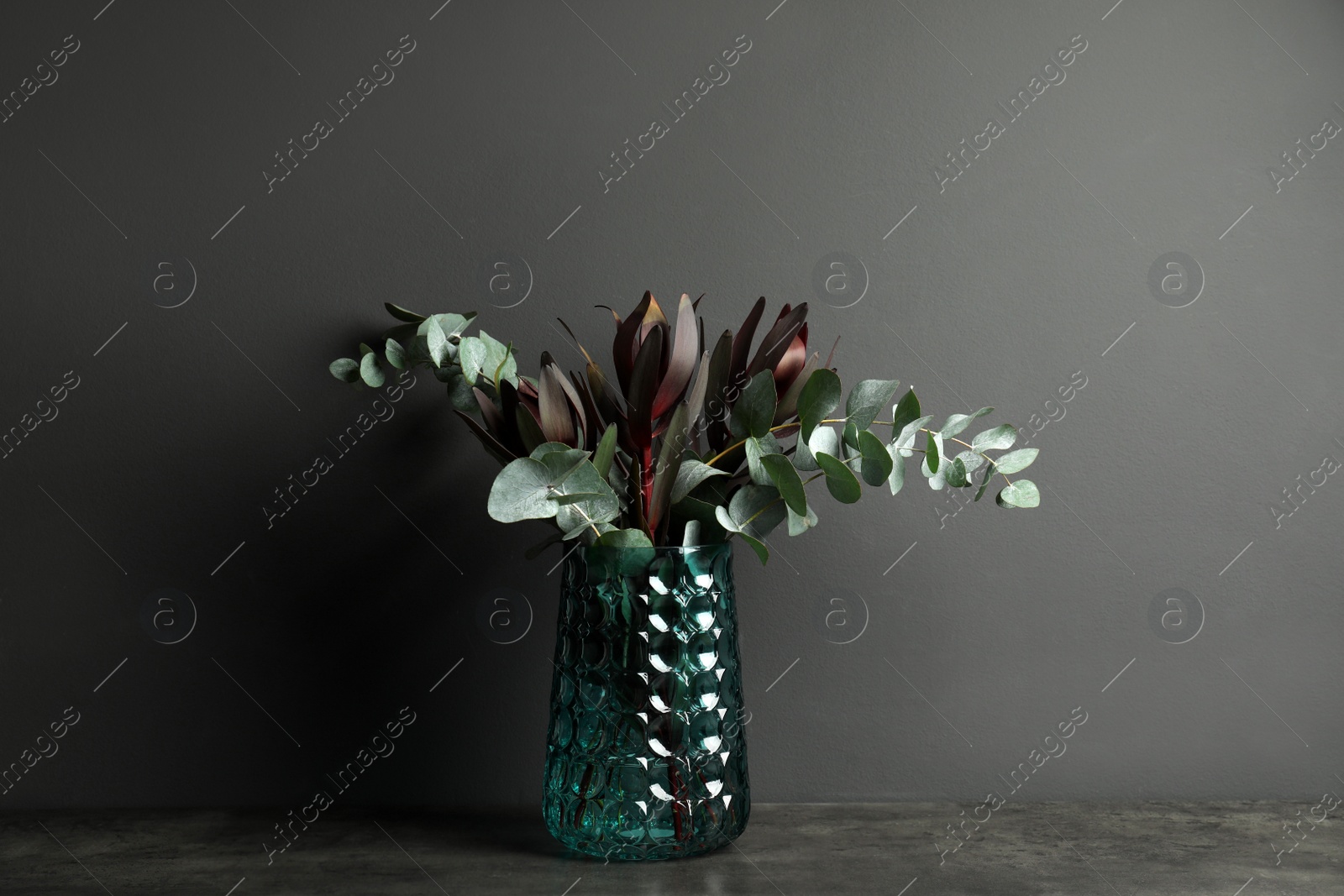 Photo of Bouquet of protea flowers and eucalyptus branches in glass vase on table against black background