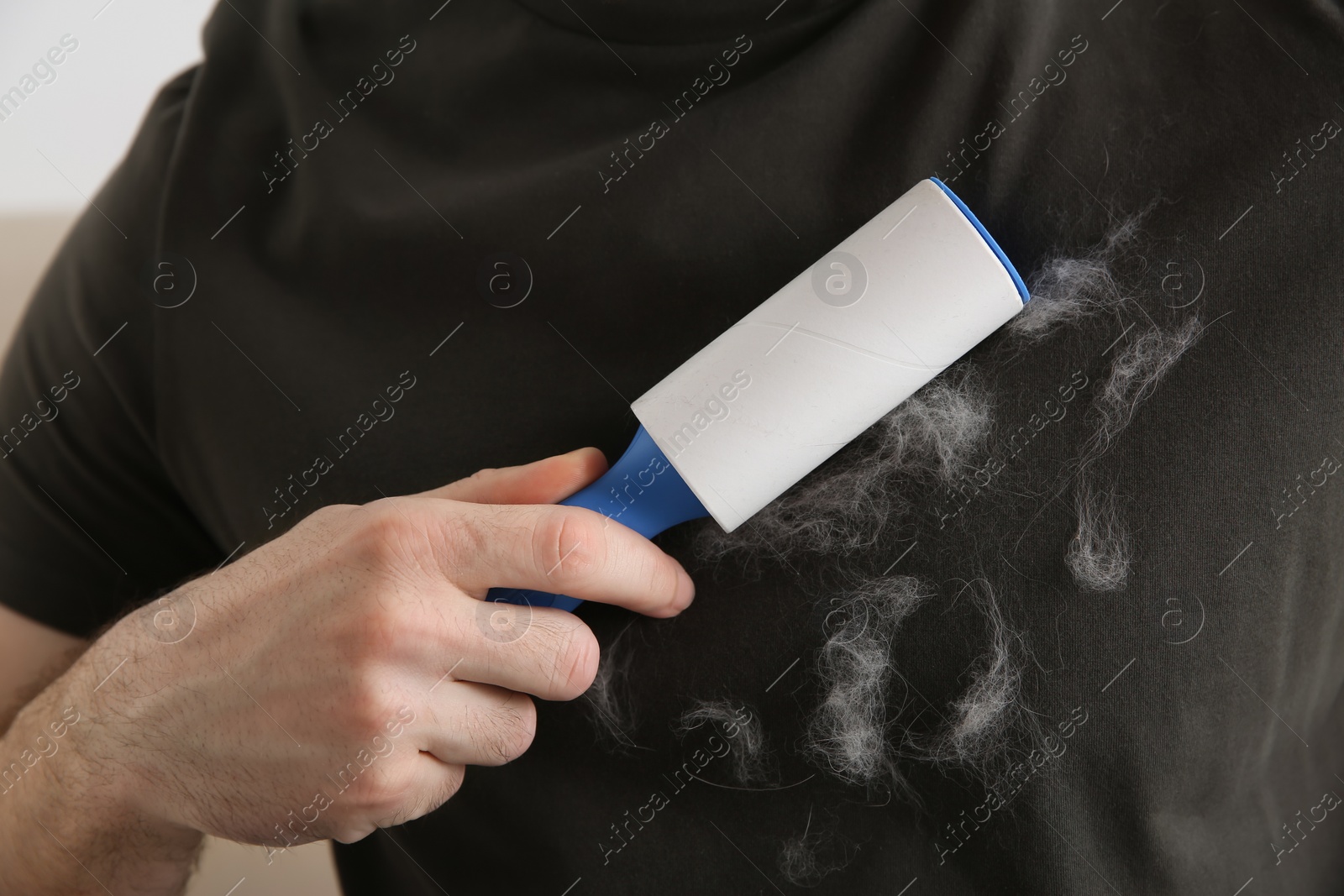 Photo of Man removing hair from grey t-shirt with lint roller on light background, closeup