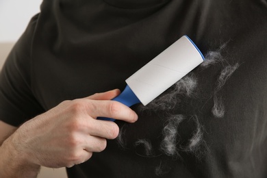 Man removing hair from grey t-shirt with lint roller on light background, closeup