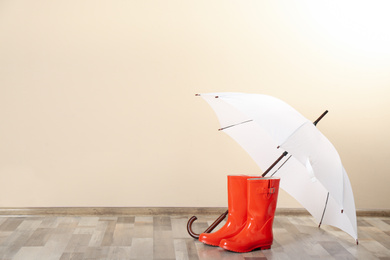 Photo of Beautiful white umbrella and rubber boots near beige wall. Space for text