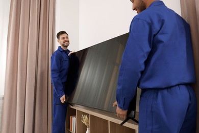 Male movers installing plasma TV near white wall in new house