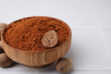 Nutmeg powder in bowl and seeds on white table, closeup. Space for text