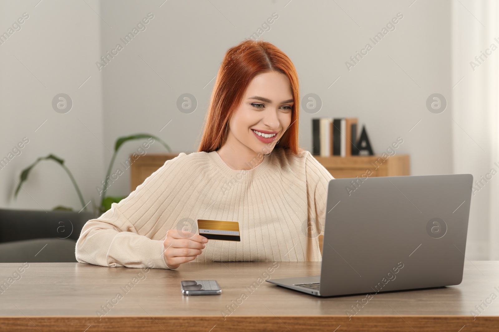 Photo of Happy woman with credit card using laptop for online shopping at wooden table in room