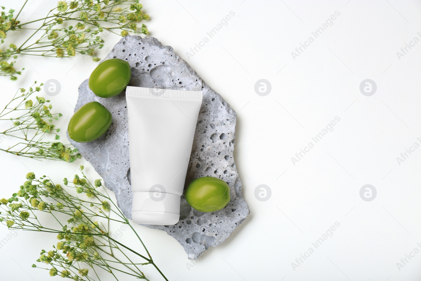 Photo of Tube of cream, olives and flowers on white background, flat lay. Space for text