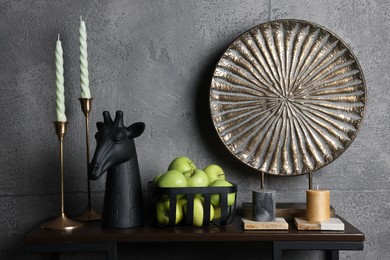 Photo of Wooden shelf with candles, decorative figure of giraffe, plate and apples against grey wall