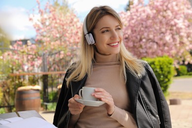 Photo of Happy woman listening to audiobook in outdoor cafe