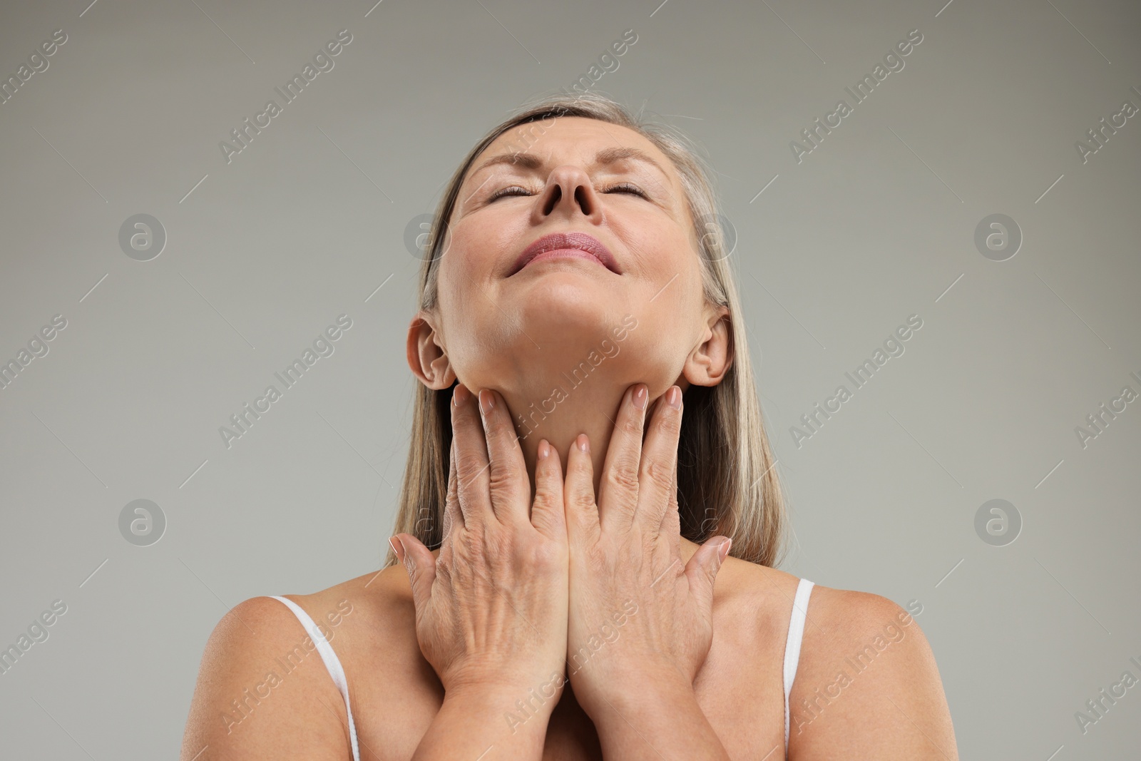 Photo of Beautiful woman touching her neck on grey background, low angle view