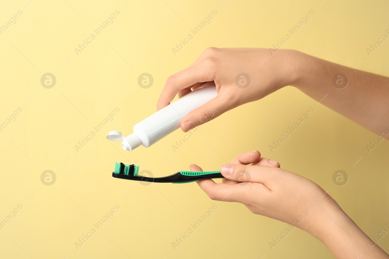 Photo of Woman squeezing toothpaste on brush against color background