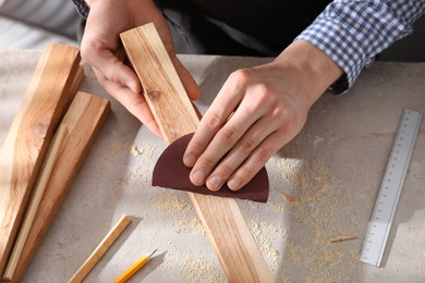 Man polishing wooden plank with sandpaper at grey table, closeup