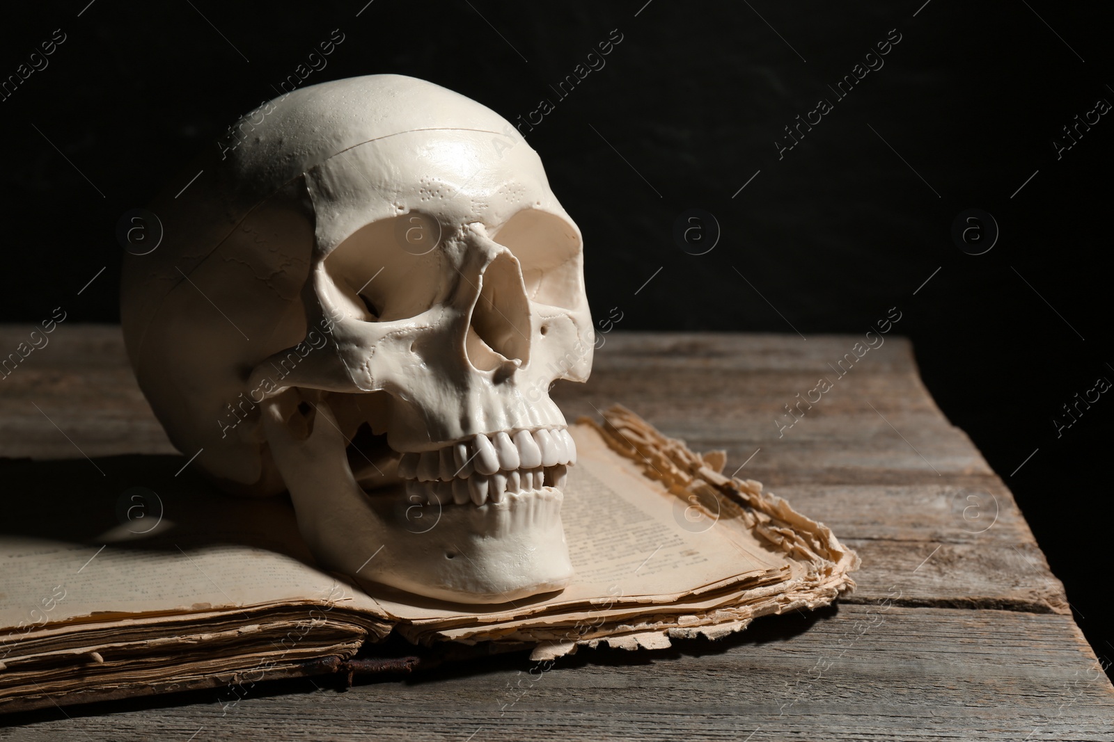 Photo of Human skull and old book on wooden table against black background, space for text