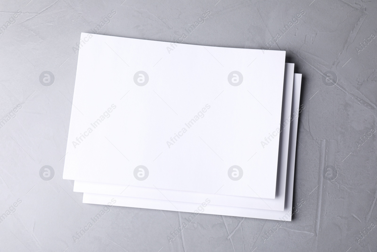 Photo of Blank paper sheets on light grey stone background, top view. Mock up for design