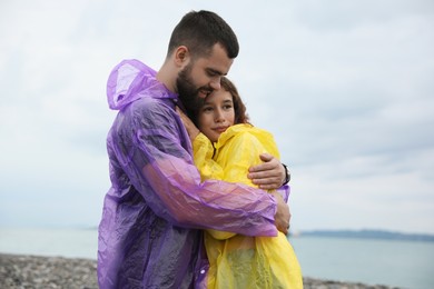 Photo of Young couple in raincoats enjoying time together under rain on beach