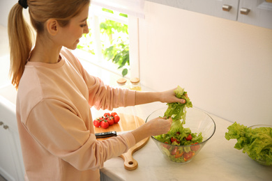 Young woman cooking salad at table in kitchen, focus on hands