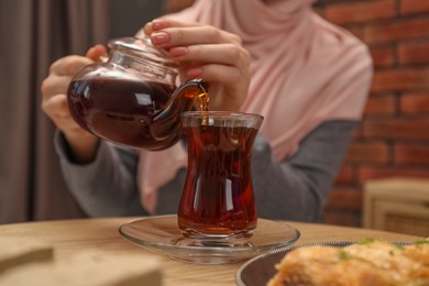 Woman pouring delicious Turkish tea from teapot into cup at wooden table, closeup