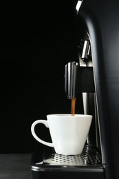 Photo of Modern espresso machine pouring coffee into cup on grey table against black background
