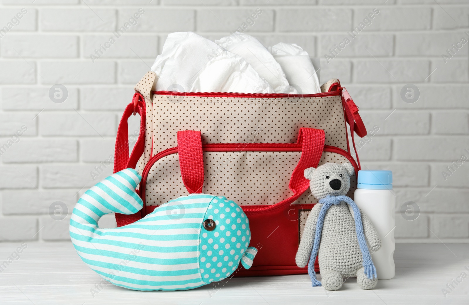 Photo of Bag with diapers and baby accessories on wooden table against white brick wall