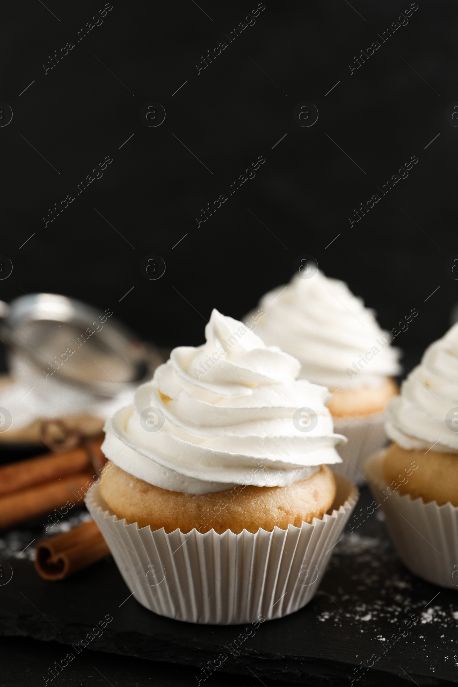 Photo of Delicious cupcakes with cream and cinnamon on slate board, closeup