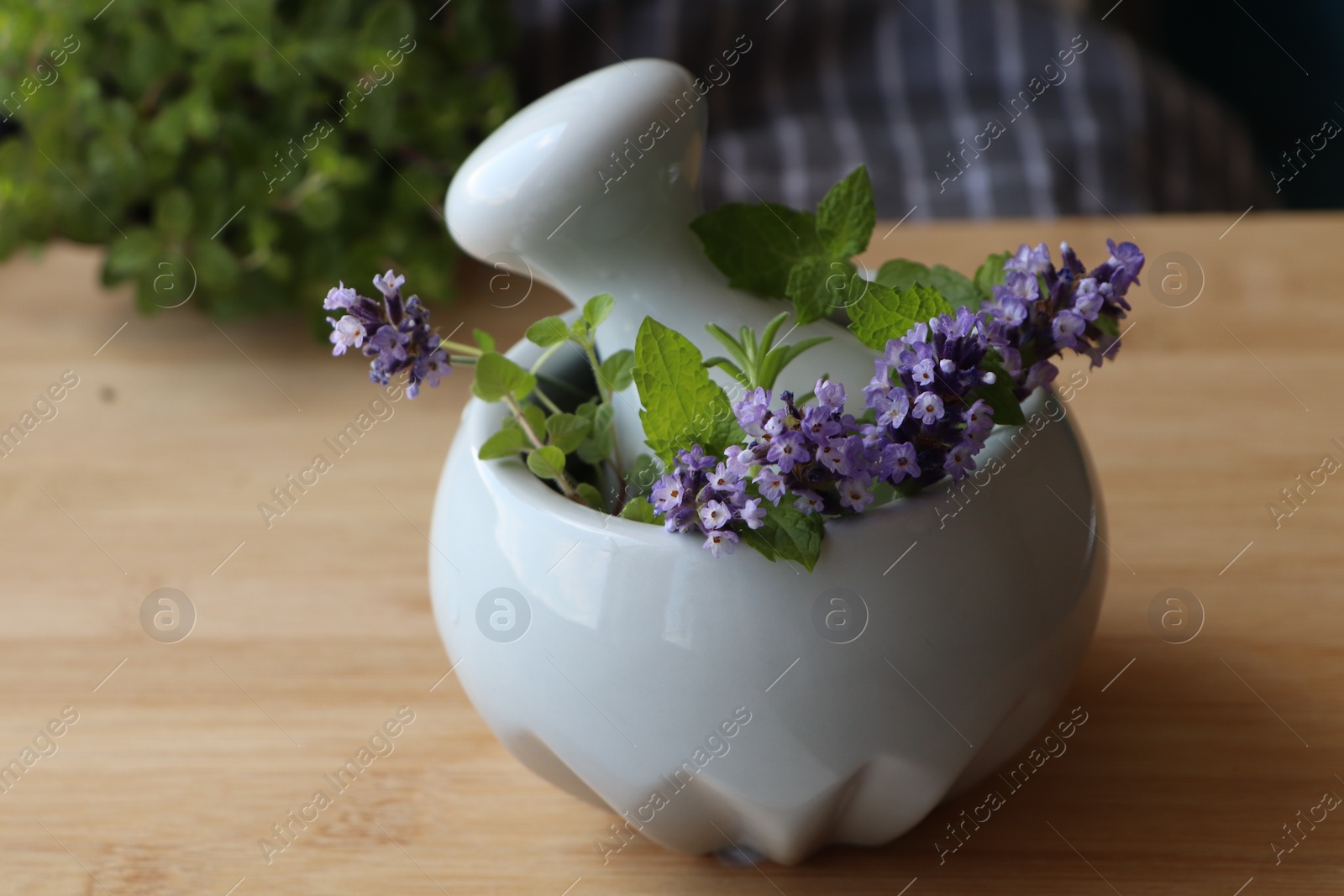 Photo of Mortar with fresh lavender flowers, herbs and pestle on wooden table