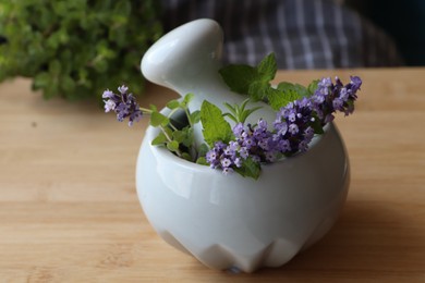 Mortar with fresh lavender flowers, herbs and pestle on wooden table