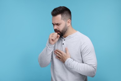 Sick man coughing on light blue background