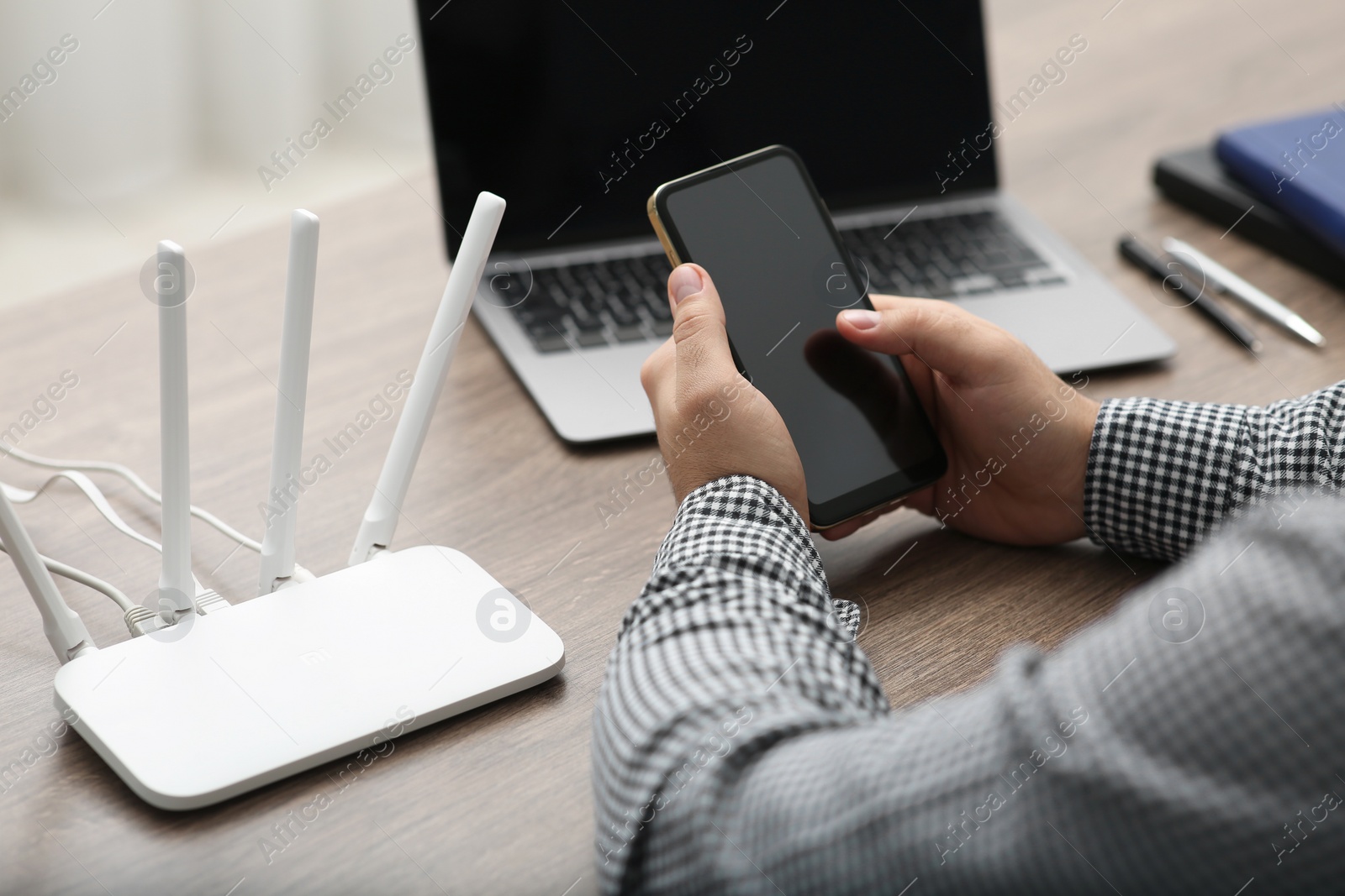 Photo of Man with smartphone and laptop connecting to internet via Wi-Fi router at wooden table, closeup