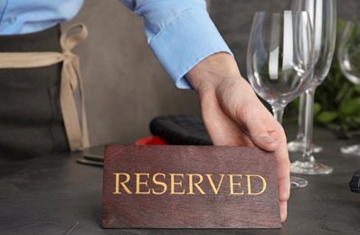 Photo of Waiter setting RESERVED sign on restaurant table, closeup